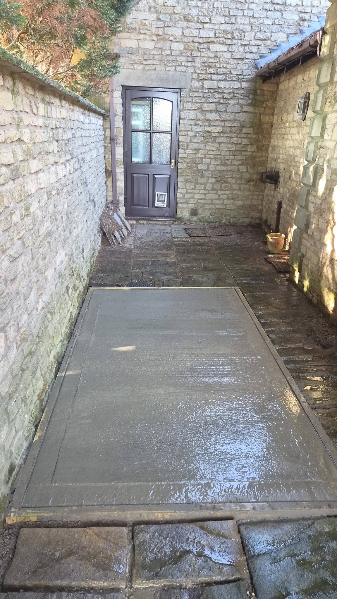 A fresh concrete base laid in a narrow passage between old stone walls