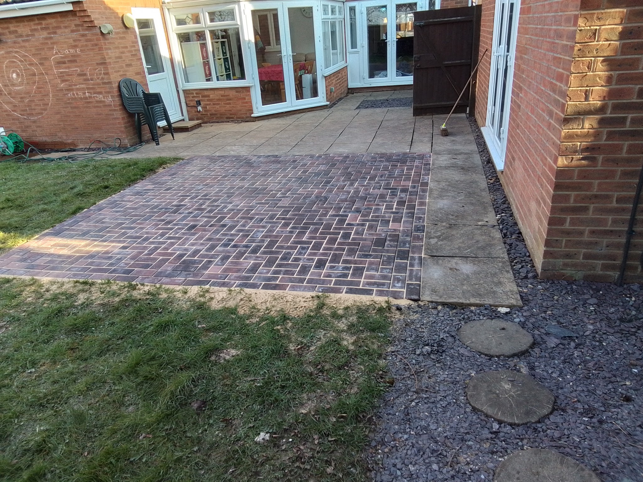 A red block-paved path leading to a patio at the back of a brick house