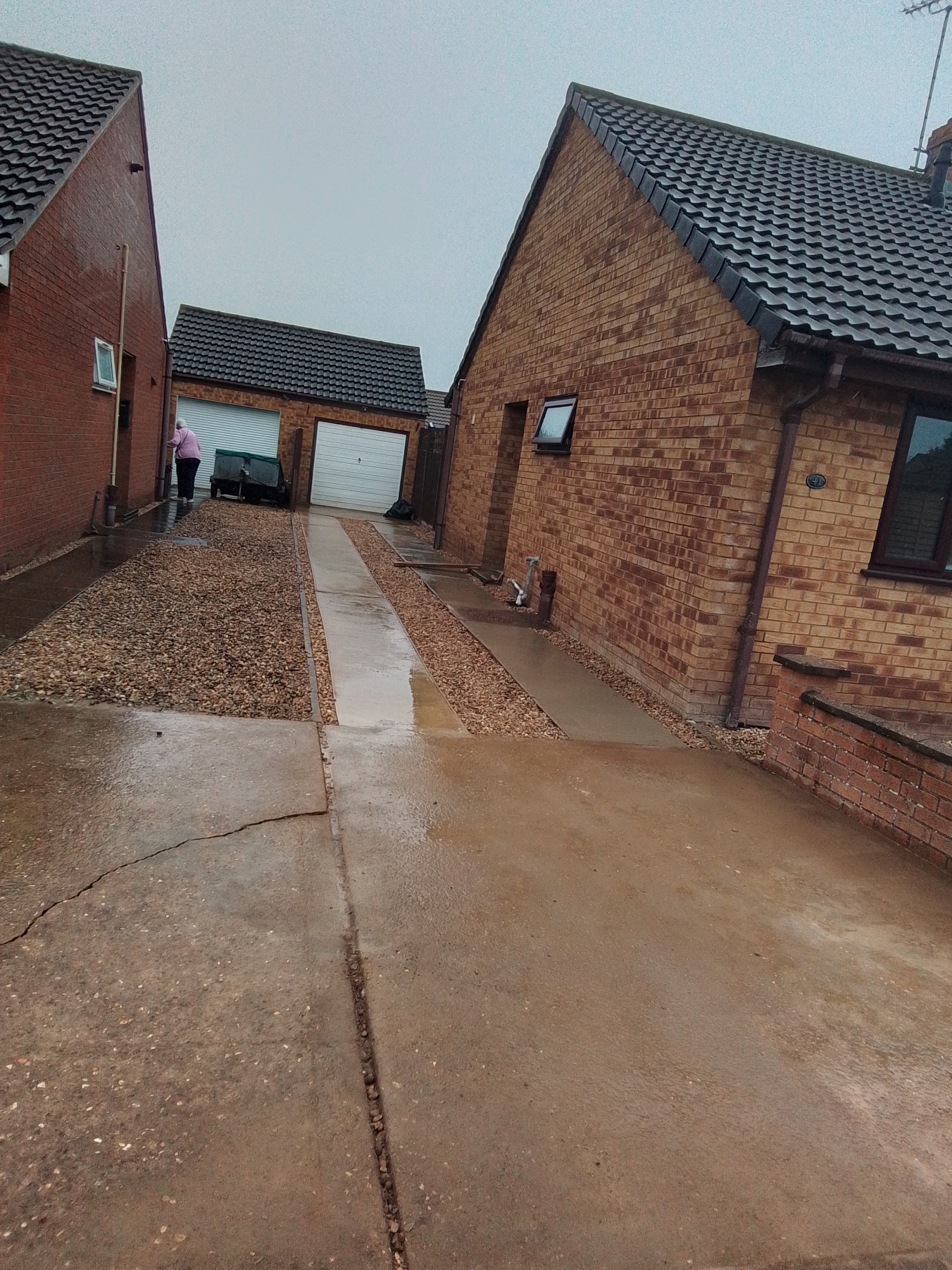 A long concrete driveway running between two brick bungalows to a double garage